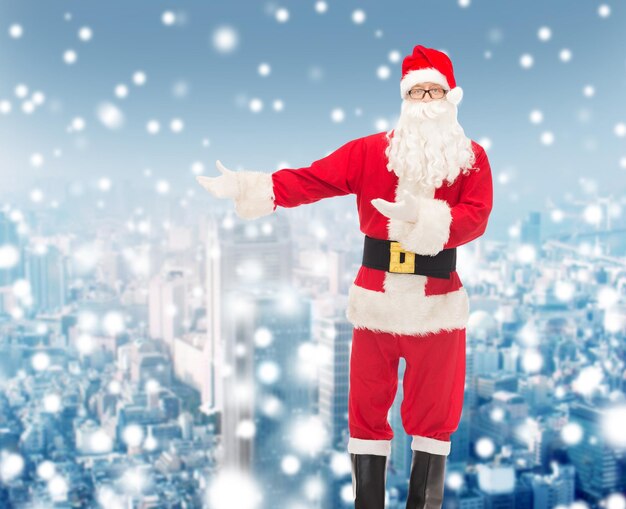 concepto de navidad, vacaciones, gestos y personas - hombre disfrazado de santa claus sobre fondo de ciudad nevada