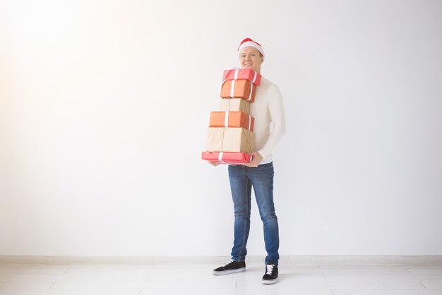 Concepto de Navidad y vacaciones hombre con gorro de Papá Noel sosteniendo la pila de cajas de regalo sobre fondo blanco.