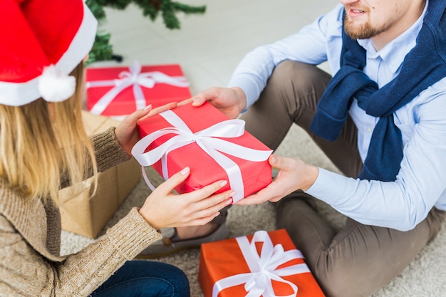 Concepto de Navidad y vacaciones - joven pareja feliz con gorro de Papá Noel abriendo regalos en casa.