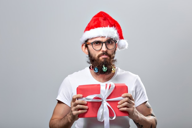 Concepto de Navidad, vacaciones, peluquería y estilo - joven apuesto hombre barbudo de santa claus con muchos pequeños adornos navideños en barba larga.