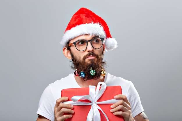 Concepto de Navidad, vacaciones, peluquería y estilo - joven apuesto hombre barbudo de santa claus con muchos pequeños adornos navideños en barba larga.