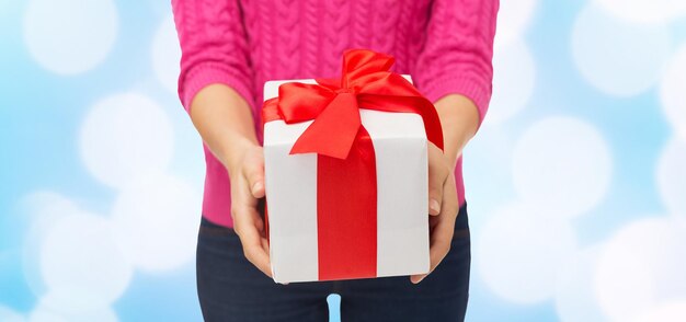 concepto de navidad, vacaciones y personas - cerca de una mujer con suéter rosa sosteniendo una caja de regalo sobre fondo de luces azules