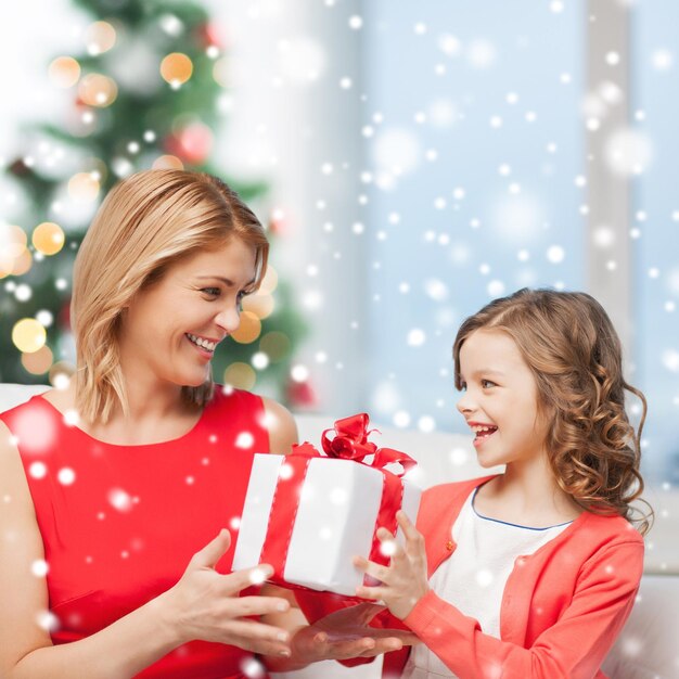 concepto de navidad, vacaciones, personas y familia - madre e hija sonrientes con caja de regalo en casa