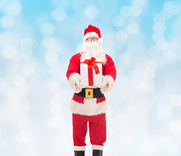 concepto de navidad, vacaciones y personas - hombre disfrazado de santa claus con caja de regalo sobre fondo de luces azules