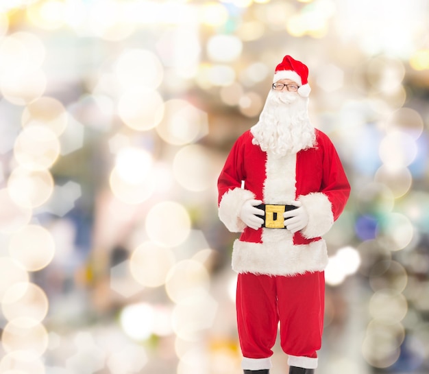 concepto de navidad, vacaciones y personas - hombre disfrazado de santa claus sobre fondo de luces