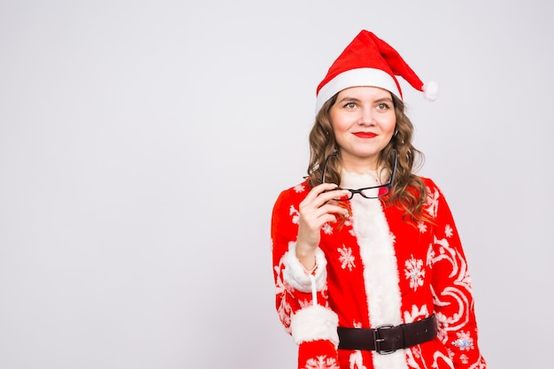 Concepto de Navidad, vacaciones y personas - mujer joven en traje de santa se quitó las gafas en la pared blanca con espacio de copia.