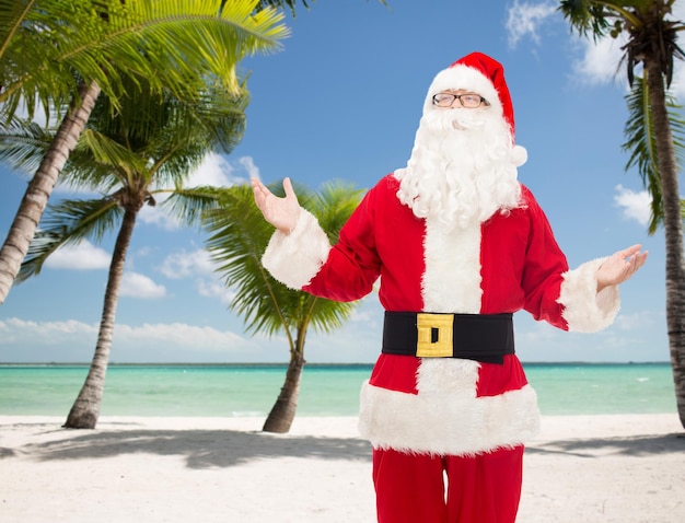 Foto concepto de navidad, vacaciones, viajes y personas - hombre disfrazado de santa claus sobre fondo de playa tropical