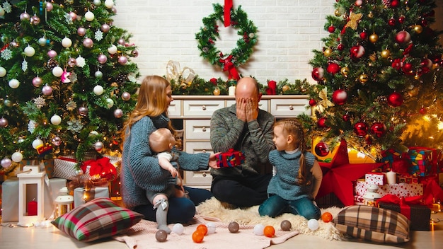 Concepto navideño familia feliz se sienta en el ambiente navideño e intercambia regalos papá sentado con los ojos cerrados
