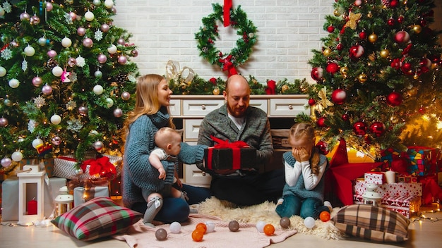 Concepto navideño familia feliz se sienta en el entorno navideño e intercambia regalos una niña sentada con los ojos cerrados