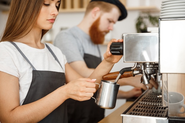 Concepto de negocio del café - retrato de la señora barista en el delantal que prepara y que hierve la leche para la orden del café con su socio mientras que se coloca en el café.