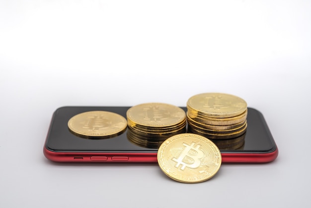 Concepto de negocio, dinero, tecnología y criptomoneda. Primer plano de monedas de oro bitcoin en teléfono inteligente móvil rojo con fondo blanco.