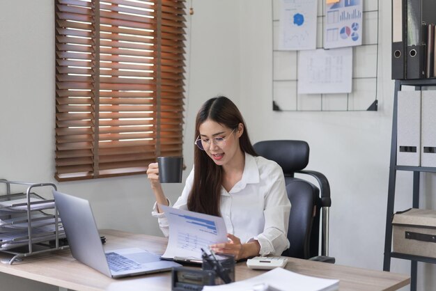 Concepto de negocio Empresaria está leyendo documentos financieros y bebiendo café en la oficina moderna