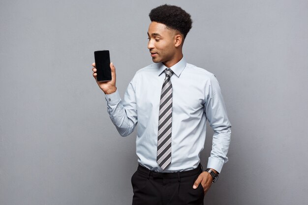 Concepto de negocio - empresario afroamericano profesional guapo feliz mostrando el teléfono móvil al cliente.