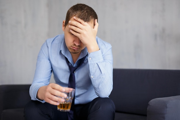 Concepto de negocio y estrés de alcoholismo joven empresario bebiendo whisky en casa u oficina
