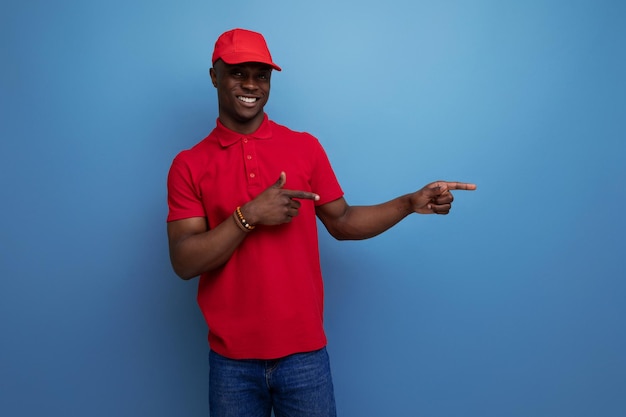 Concepto de negocio exitoso feliz joven repartidor hombre americano en camiseta roja y gorra de béisbol