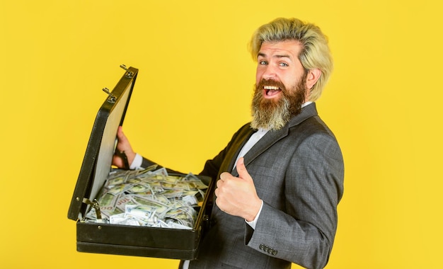 Concepto de negocio exitoso hombre rico con barba vive en una bolsa de lujo con un dólar hombre feliz y exitoso tiene caja de dinero hombre barbudo muestra maletín de oficina buen negocio