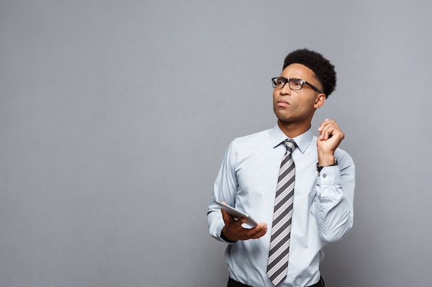 Concepto del negocio - Hombre de negocios afroamericano profesional hermoso feliz impactante y pensamiento con la tableta digital en su mano.