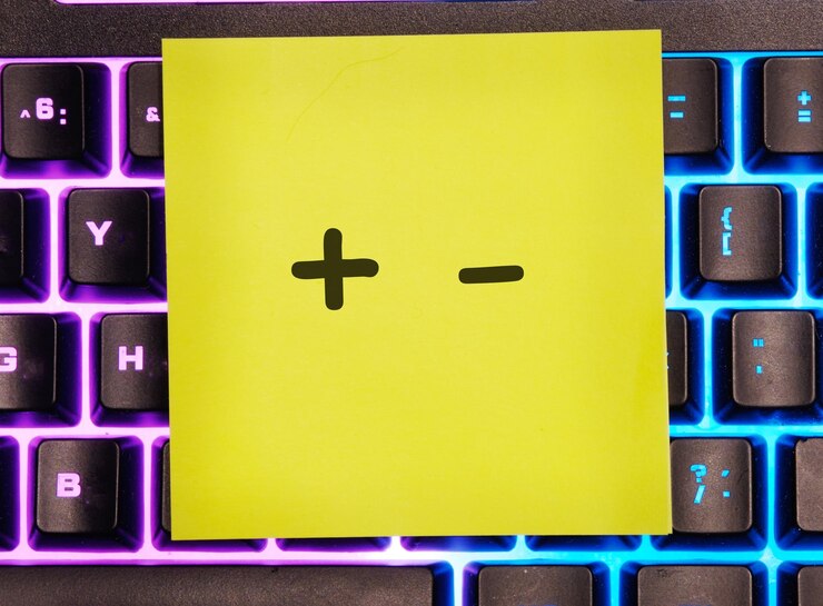 Foto concepto de negocio más menos símbolos está escrito en una pegatina amarilla en un teclado de computadora portátil con luz de fondo