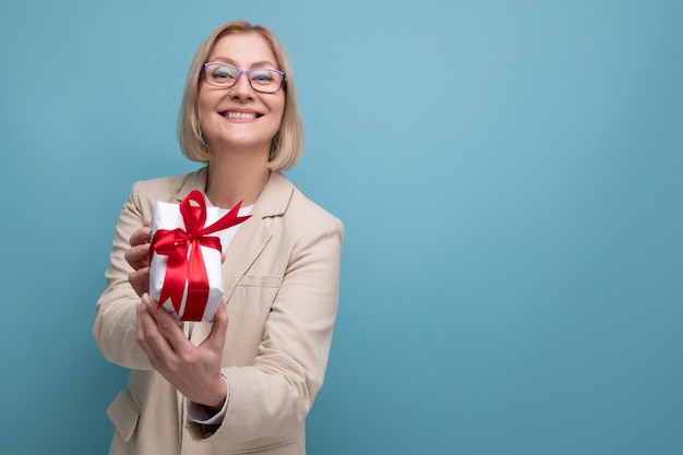 Concepto de negocio de mediana edad una mujer en una chaqueta sostiene una caja de regalo con un lazo en un fondo de estudio