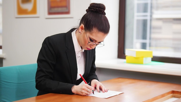 Concepto de negocio Una mujer con gafas se sienta junto a la mesa y llena los documentos