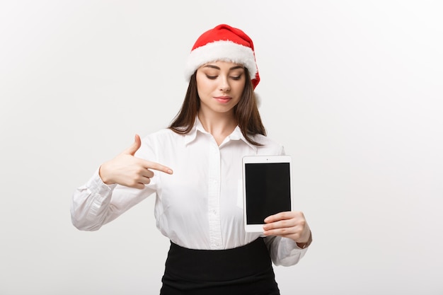 Concepto de negocio - mujer de negocios caucásica joven en tema de Navidad mostrando y apuntando a tableta digital.