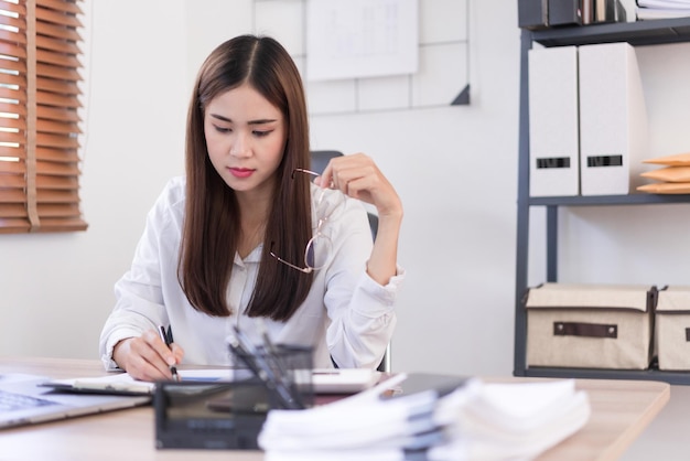 Concepto de negocio La mujer de negocios sostiene gafas mientras lee y escribe datos en un documento comercial