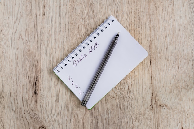 Concepto de negocio y oficina - cuaderno en blanco y lápiz negro sobre mesa de madera. Objetivos 2019. Vista plana mínima, vista superior.