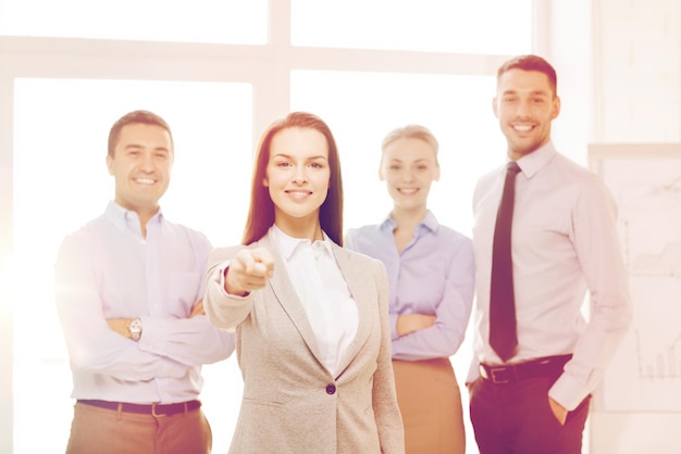 concepto de negocio y oficina - mujer de negocios sonriente y guapa con un equipo en la oficina señalándote con el dedo