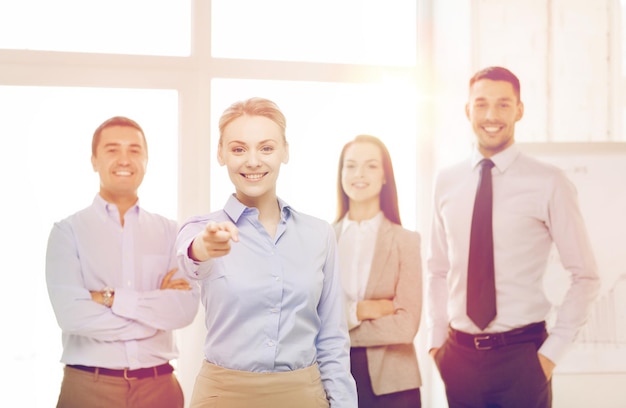 concepto de negocio y oficina - mujer de negocios sonriente y guapa con un equipo en la oficina señalándote con el dedo