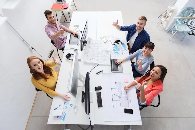 concepto de negocio, puesta en marcha, éxito y personas: equipo creativo con computadoras, planos y esquemas que muestran su aprobación en la oficina