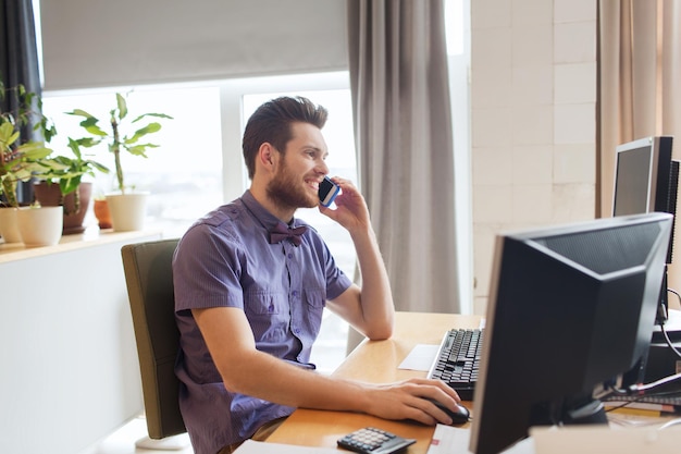 concepto de negocio, puesta en marcha y personas - hombre de negocios feliz o trabajador de oficina masculino creativo con computadora llamando a un teléfono inteligente