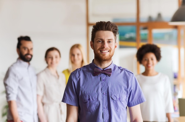 concepto de negocio, puesta en marcha, personas y trabajo en equipo - joven feliz con barba y corbata de moño sobre el equipo creativo en el cargo