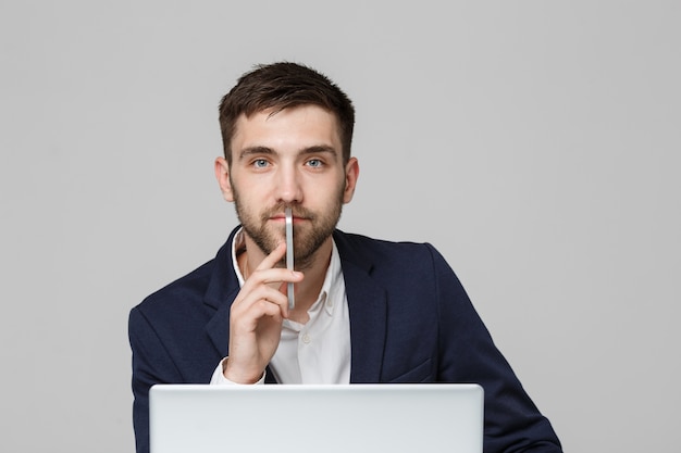 Concepto de negocio - Retrato apuesto hombre de negocios apuesto feliz en traje jugando moblie teléfono y sonriendo con portátil en la oficina de trabajo. Fondo blanco.