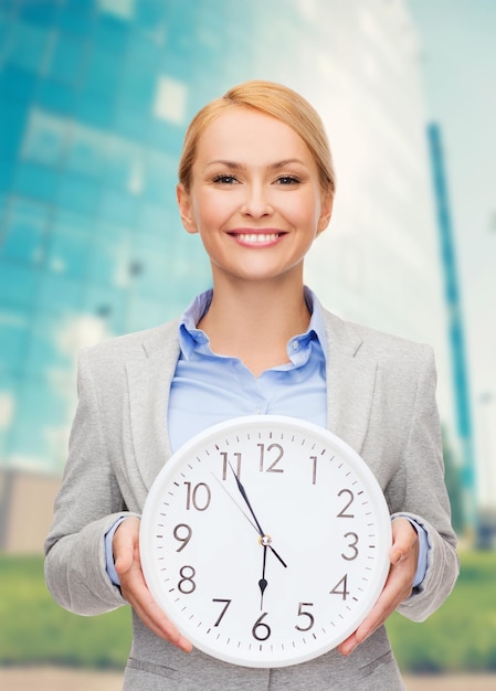 concepto de negocio y tiempo - atractiva mujer de negocios con reloj de pared