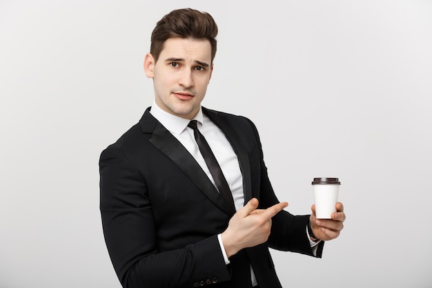 Concepto de negocio: Tiro de medio cuerpo de un apuesto hombre de negocios en un traje sosteniendo una taza de café y apuntando con su dedo
