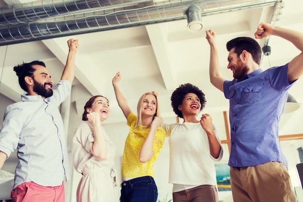 Foto concepto de negocio, triunfo, gesto, personas y trabajo en equipo - feliz equipo creativo levantando la mano y celebrando la victoria en el cargo