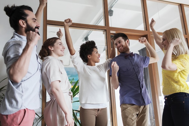 concepto de negocio, triunfo, gesto, personas y trabajo en equipo - feliz equipo creativo levantando la mano y celebrando la victoria en el cargo