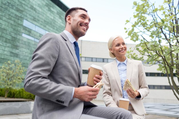 concepto de negocios, asociación, comida, bebidas y personas - hombres de negocios sonrientes con vasos de papel parados sobre el edificio de oficinas