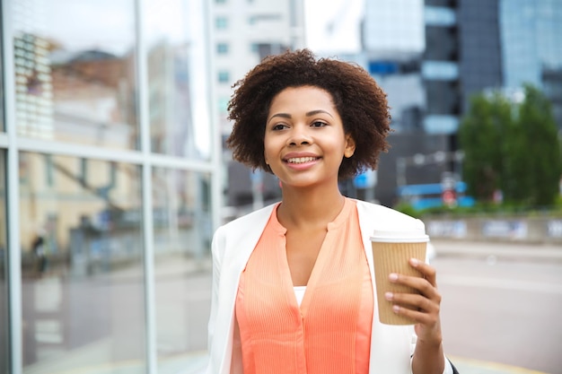 concepto de negocios, bebidas y personas - joven empresaria afroamericana sonriente con taza de café en la ciudad