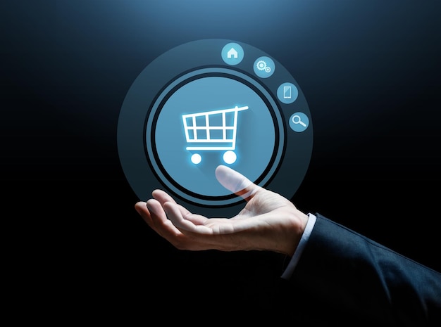 concepto de negocios, comercio electrónico y personas: primer plano de la mano de un hombre de negocios con carrito de compras sobre fondo oscuro