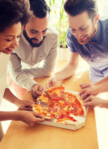 concepto de negocios, comida, almuerzo y personas - equipo de negocios feliz comiendo pizza en la oficina