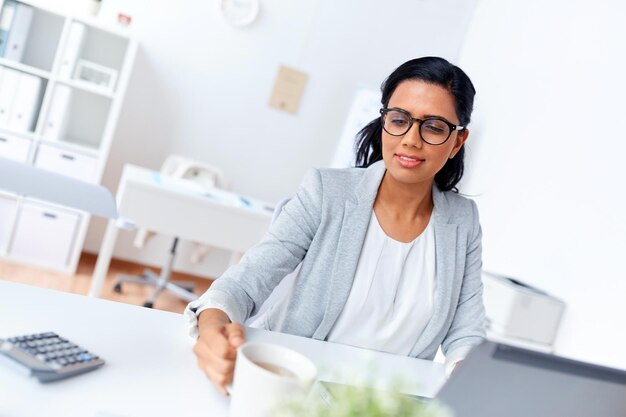 Foto concepto de negocios, descansos y personas - mujer de negocios sonriente bebiendo café o té en la oficina