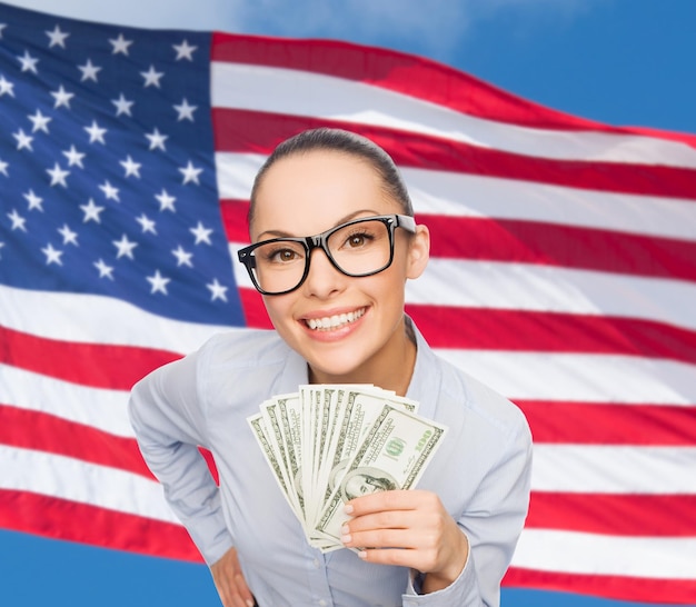 concepto de negocios, dinero y banca - mujer de negocios sonriente con anteojos con dinero en efectivo en dólares sobre el fondo de la bandera americana