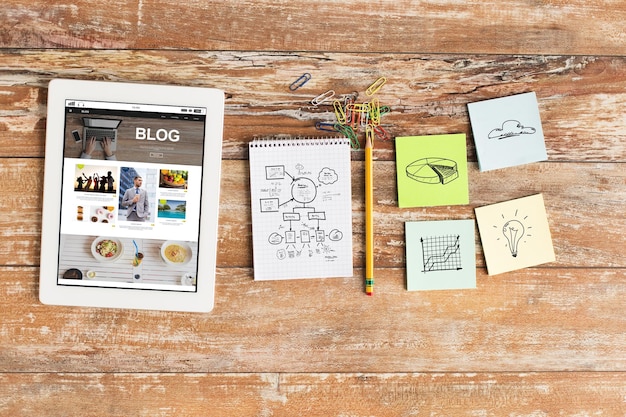 concepto de negocios, educación, objetos y tecnología - cierre de notebook, tablet pc con página web de blog en pantalla y pegatinas en la mesa