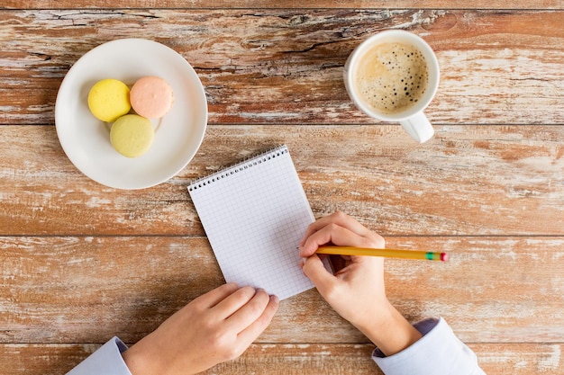 concepto de negocios, educación y personas: cierre de manos femeninas con cuaderno, lápiz, café y galletas en la mesa