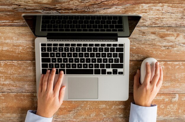 concepto de negocios, educación, personas y tecnología: cierre de manos femeninas con computadora portátil y mouse de computadora en la mesa