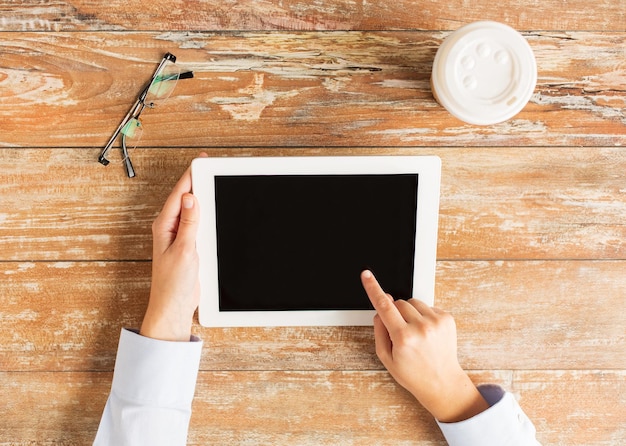 concepto de negocios, educación, personas y tecnología: cierre de manos femeninas que señalan con el dedo a la pantalla en blanco negra de la computadora de la tableta con taza de café y anteojos