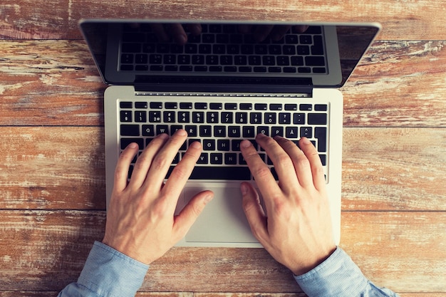 concepto de negocios, educación, personas y tecnología - cierre de manos masculinas con laptop en la mesa