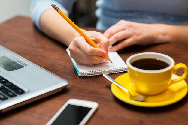 concepto de negocios, educación, personas, tecnología y estilo de vida: cierre de una mujer escribiendo en un cuaderno con lápiz