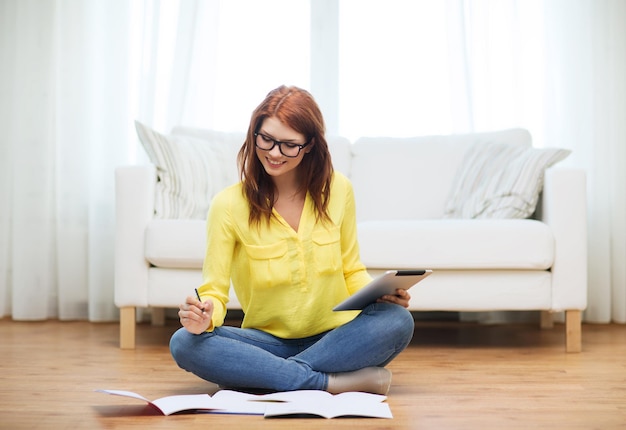 concepto de negocios, educación y tecnología - estudiante sonriente en anteojos con cuadernos y computadora de tablet pc en casa